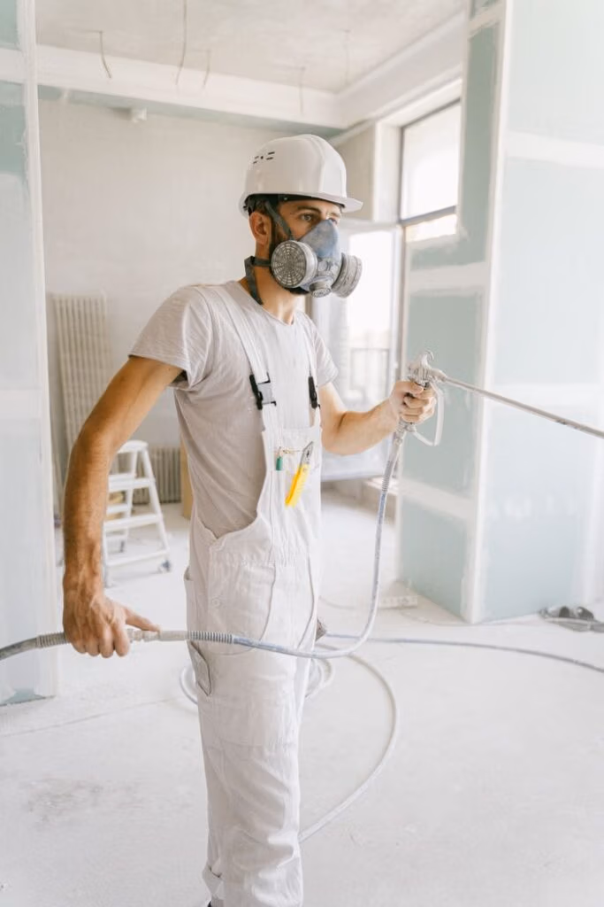 A construction worker wearing a gas mask and holding a hose in a renovation site.